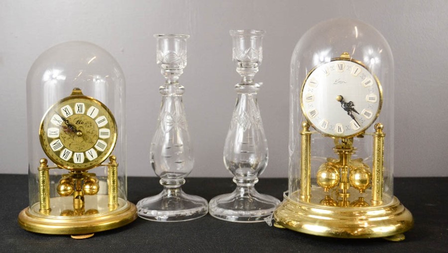 A pair of glass candlesticks and two brass mantle clocks with glass domes.