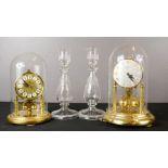 A pair of glass candlesticks and two brass mantle clocks with glass domes.