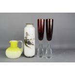 Two red glass champagne flutes, a white opaque vase and yellow jug.