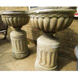 Two reconstituted stone garden urns, raised on pedestals.