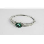 A silver bangle set with an emerald coloured glass stone.