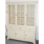 A painted glazed dresser with three glass fronted cupboards above drawers and cupboard doors.