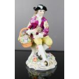 A Sitzendorf porcelain male figure seated and holding a basket of flowers, 12cm high.