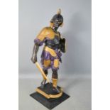 A cast metal figure of a Roman soldier, painted with detail, raised on a plinth, 47cm high.