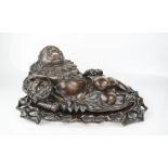 A 19th century hardwood carved smiling buddha and dragon, in reclined position, raised on a carved