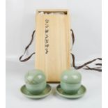 A pair of Korean celadon glazed tea bowls, and saucers with tea strainers, by Kim, b.1958, with