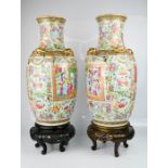 A pair of 19th century Canton famille rose vases, raised on carved wooden stands, 46cm high.