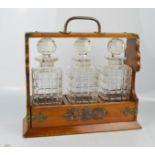 An antique oak tantalus, brass clad, with key, and three cut glass decanters.