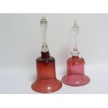 Two cranberry glass hand bells with clear glass handles (both lacking clappers), 29cm & 31.5cm high.