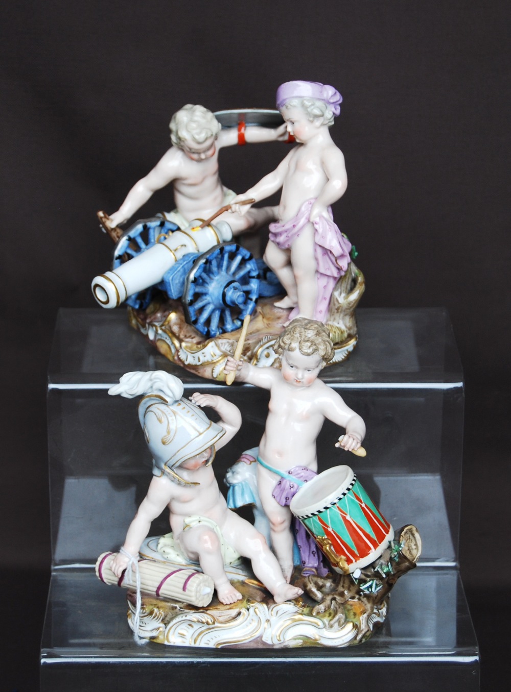 Pair of Meissen figure groups, each of two semi clad children playing at soldiers, one group with