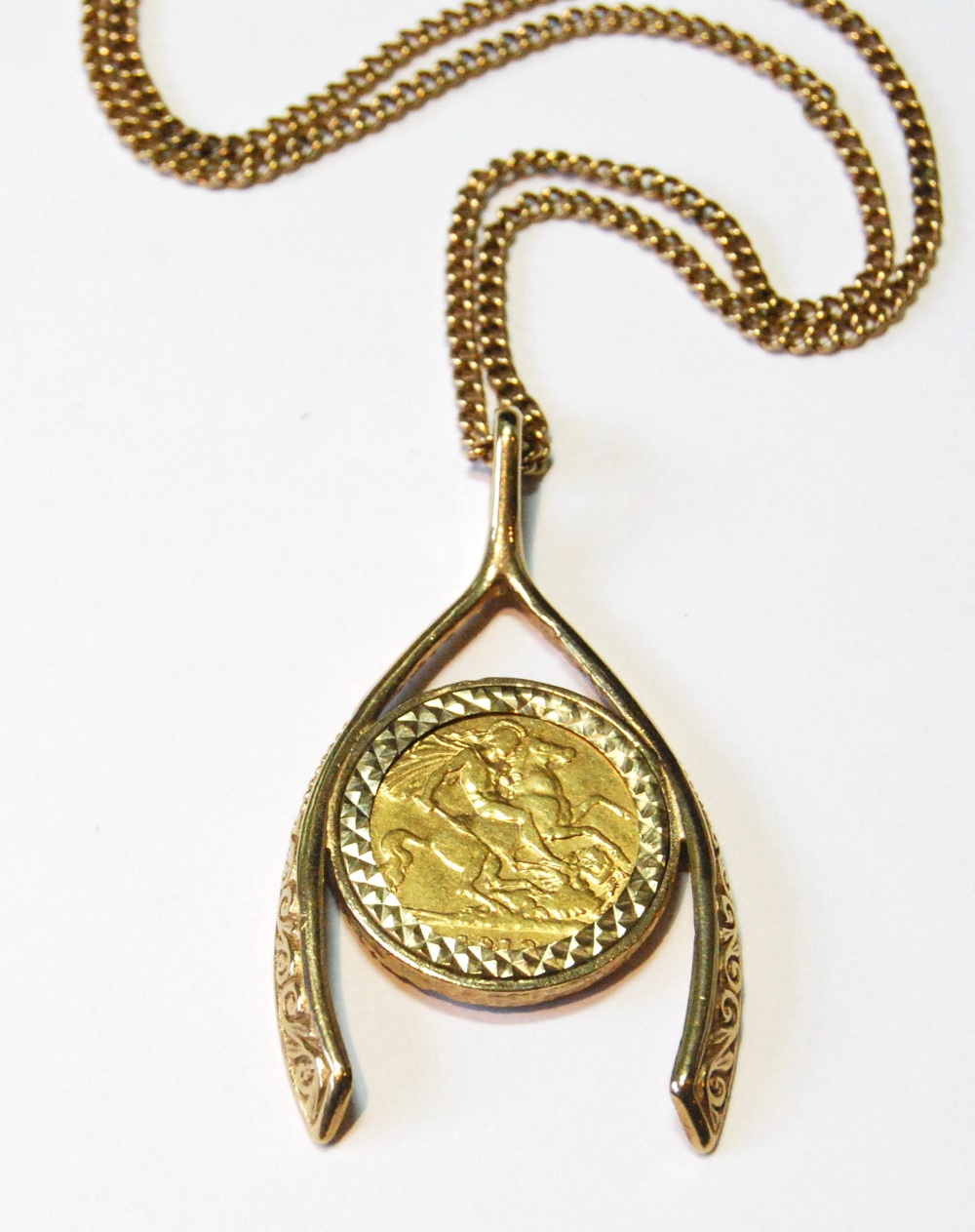 9ct gold pendant modelled as a wishbone enclosing a detachable half sovereign, 1913, 18g.