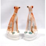 Pair of Staffordshire seated greyhounds, each with a hare at their feet, 21.5cm high.