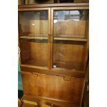 Mid century teak cabinet on stand, glazed doors over fall-flap enclosing glass shelves, stepped base