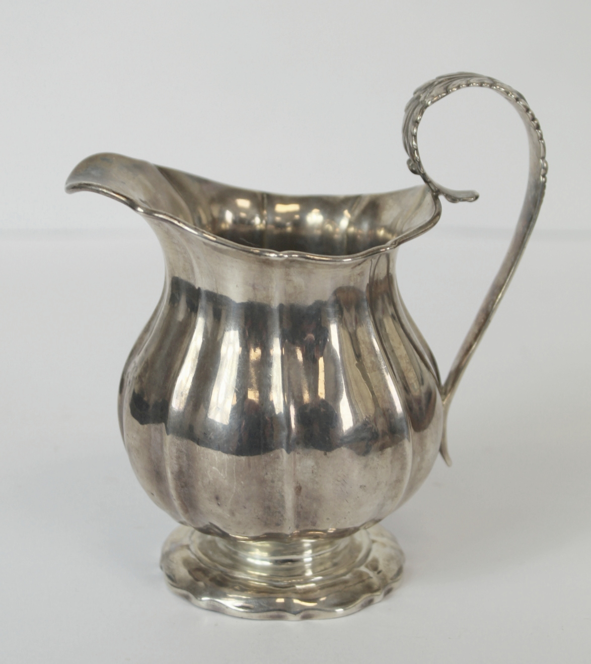 Silver cream jug of fluted baluster form with leafage handle on spreading foot, markers mark rubbed,