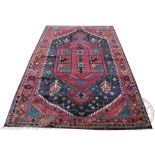 A Iranian Qashqai hand woven wool carpet, worked with a medallion design against a claret ground,