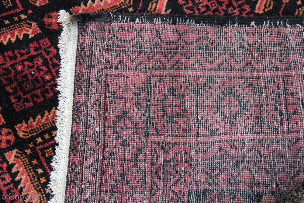 A Persian hand woven wool Baluch tribal carpet, worked with a diamond design in reds and blacks, - Image 3 of 3