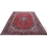 A large hand woven wool Iranian Kashan carpet, worked with medallion design against a red ground,