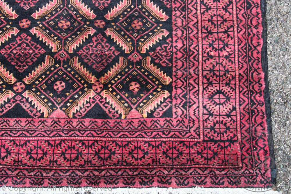 A Persian hand woven wool Baluch tribal carpet, worked with a diamond design in reds and blacks, - Image 2 of 3