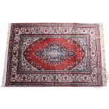 A 20th century Qum style mat, worked with a floral blue medallion against a pale red ground,