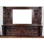 A late Victorian carved oak over mantle mirror, decorated with flowers and moustached men,