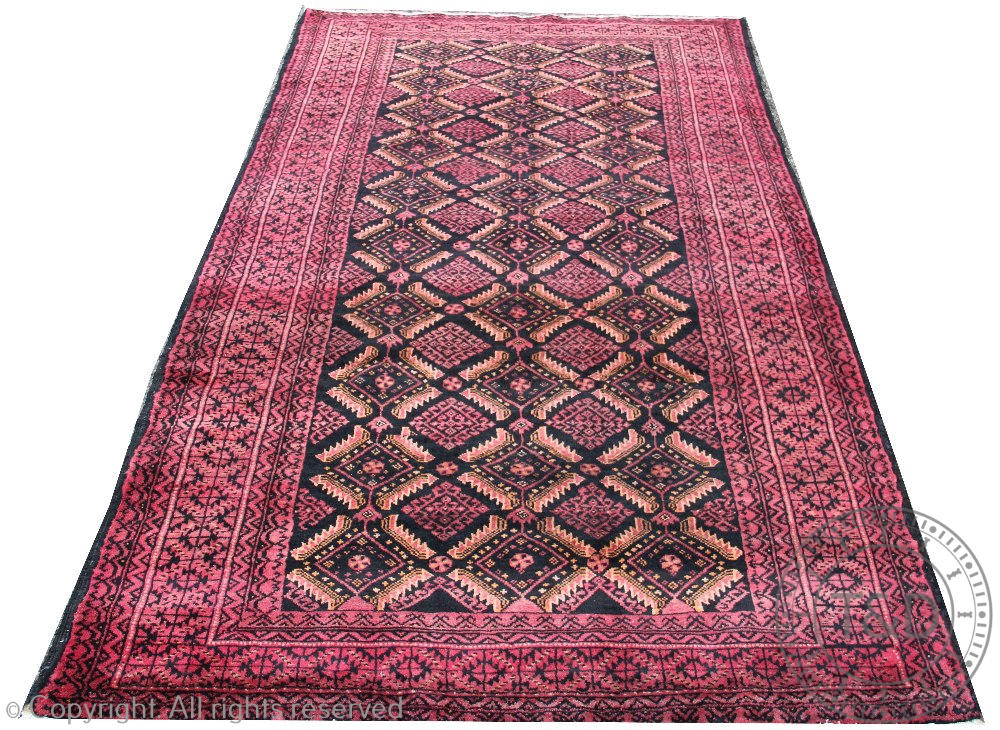A Persian hand woven wool Baluch tribal carpet, worked with a diamond design in reds and blacks,