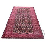 A Persian hand woven wool Baluch tribal carpet, worked with a diamond design in reds and blacks,
