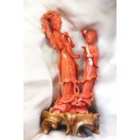 A Chinese coral carving of two figures, possibly Lan Caihe and attendee, upon a carved wood base,