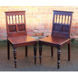 A pair of Edwardian walnut hall chairs, with panelled backs and solid seats, on turned legs,