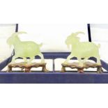 A pair of Chinese carved green stone models of goats, each modelled standing on a carved wood base,