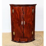 A George III mahogany bow front hanging corner cabinet, with three drawers to the base,