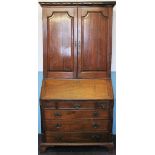 A George III oak bureau cabinet, with dentil cornice above two panelled doors,