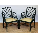 A pair of Regency style green faux bamboo painted wood chairs, with caned seats and shaped arms,