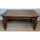 An Edwardian oak extending dining table, with canted corners, on fluted baluster legs,