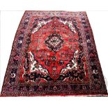A Persian full pile wool sarouk carpet, worked with a central floral medallion against a red ground,