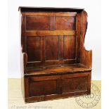 A mid 18th century Welsh oak wing back settle, with hinged seat above a box base (height reduced),