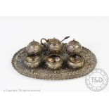 An Indian white metal miniature condiment set, each piece decorated with scroll foliage,