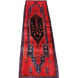 An Iranian hand woven wool runner, worked with a central blue medallion against a red ground,