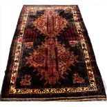 A Persian wool tribal rug, worked with two medallions against a dark ground,