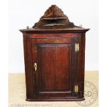 A George III oak hanging corner cupboard, with panelled door enclosing serpentine shelves,