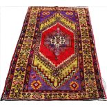 A Persian wool village rug, worked with a geometric gull against a vibrant ground with red,