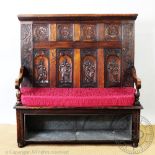 A late Victorian carved oak settle, the back panels decorated with arches enclosing various figures,