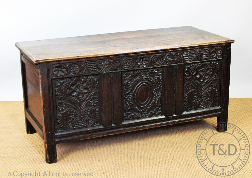 An 18th century oak coffer, with carved and panelled front, on stile legs,