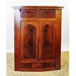 An early 19th century mahogany bow front corner cupboard, with two arched panelled doors,