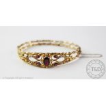 A 9ct gold garnet and seed pearl set hinged bangle,