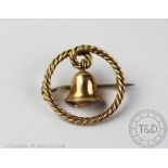 A yellow metal 'bell' brooch, designed as a rope twist circular brooch suspending a central bell,