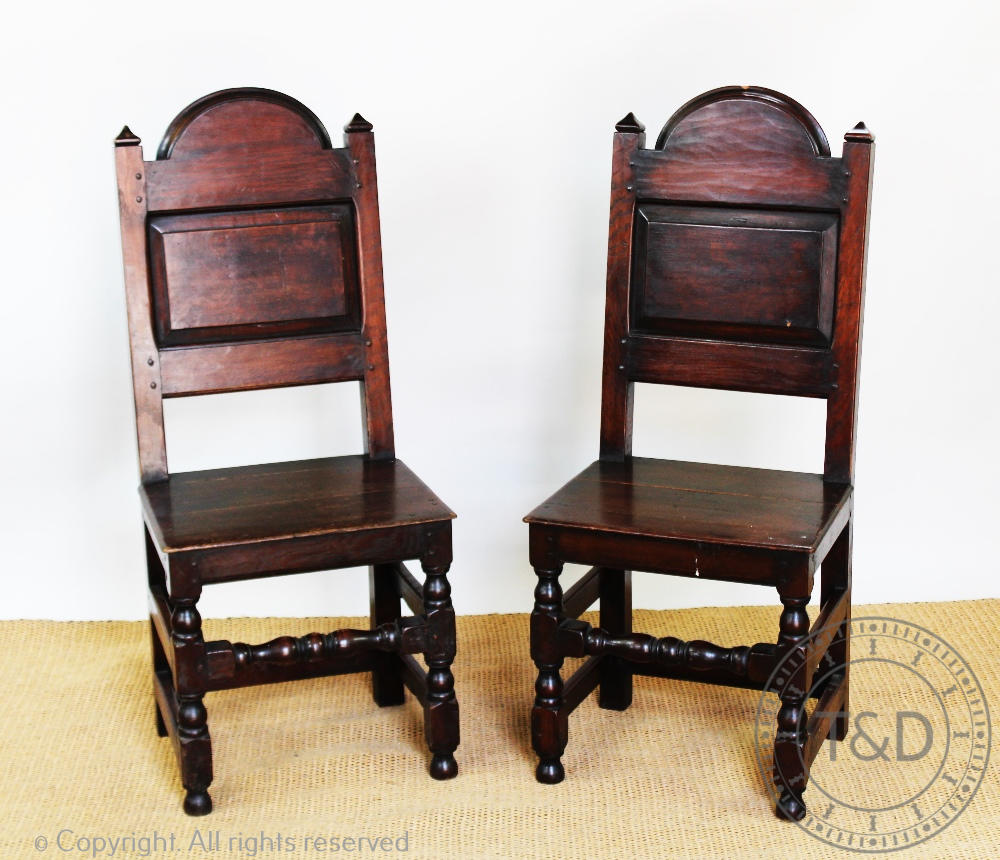 A pair of 17th century style dining chairs, with panelled backs and solid seats,