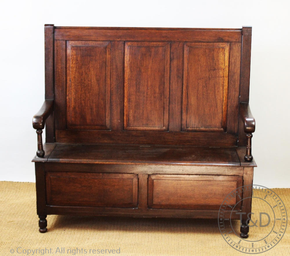 An 18th century style oak settle, with three panelled back above a box seat with hinged lid,