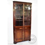 An early 19th century mahogany freestanding corner cupboard, with a moulded cornice above a pair