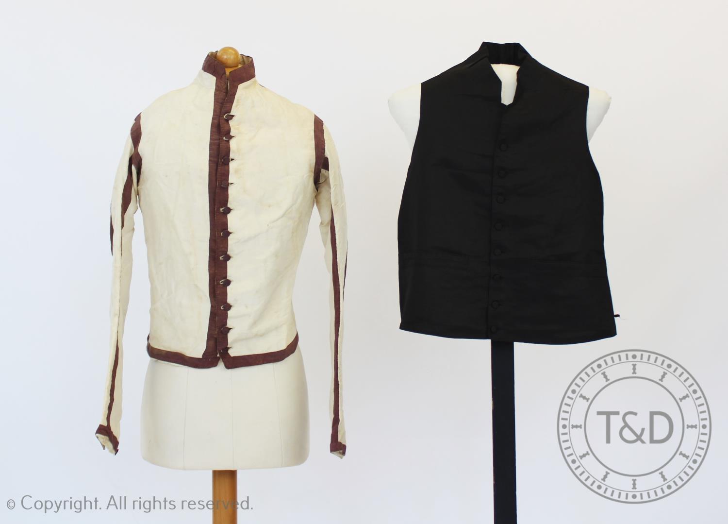 An ivory silk taffeta sleeved waistcoat or jacket, circa 1810, boldly banded and edged in dark plum,