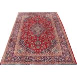 A large Persian Kashan carpet, decorated with a traditional medallion design against a red ground,